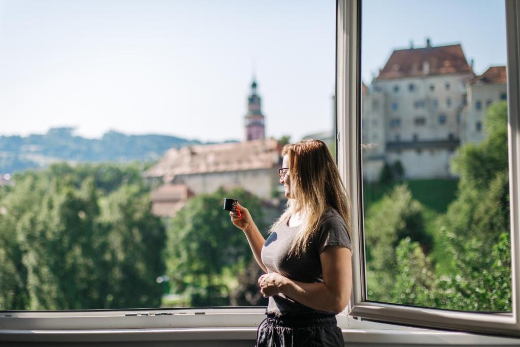 捷克克鲁姆洛夫CK-Apartment的站在窗户前看着手机的女人
