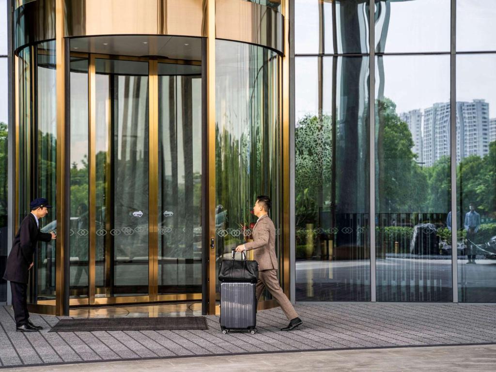杭州杭州英冠索菲特酒店的带着手提箱走过玻璃建筑的人