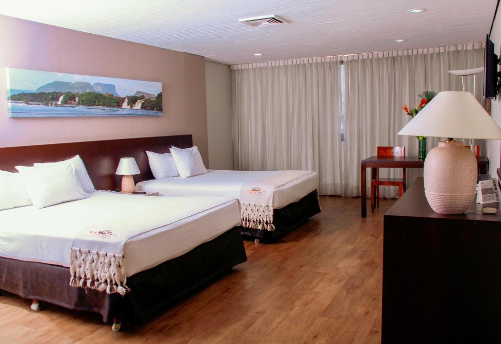 加拉加斯Hotel CCT Caracas的酒店客房设有两张床和一张桌子。
