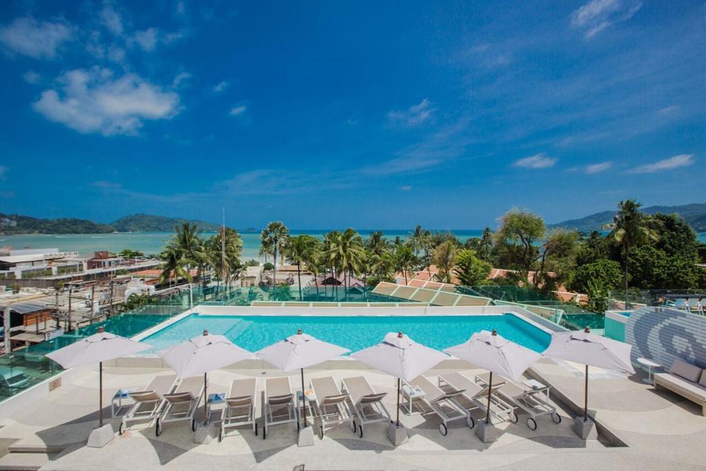 芭东海滩The Bloc Hotel - SHA Extra Plus的一个带白色遮阳伞和椅子的游泳池以及大海