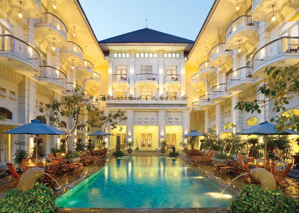 日惹The Phoenix Hotel Yogyakarta - MGallery Collection的一座带桌子和遮阳伞的室内游泳池