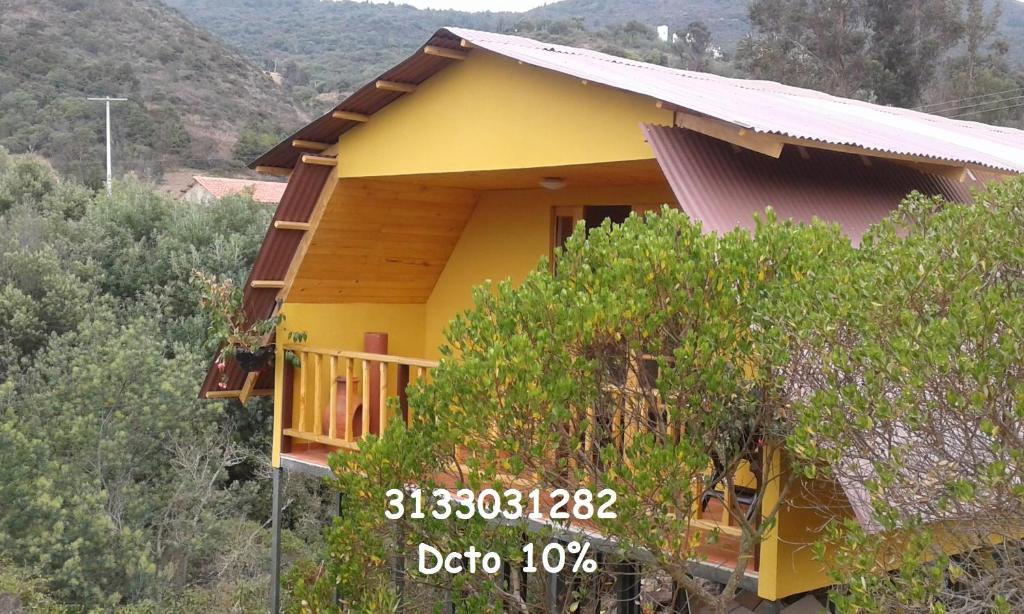 瓜塔维塔Cabaña Los Llanitos Guatavita的一座种有树木的山丘上的黄色房子