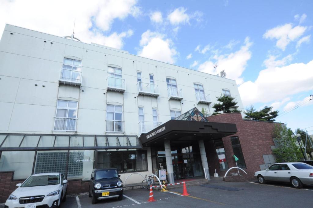 旭川高砂温泉日式旅馆的白色的建筑,有汽车停在停车场