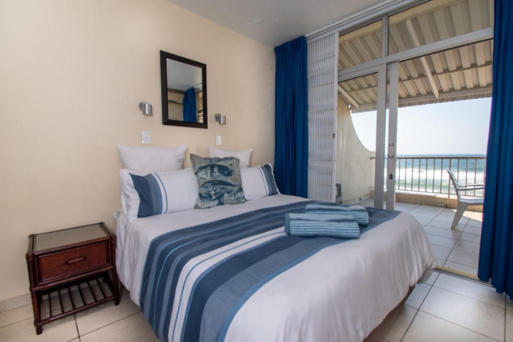德班10 Bronze Bay Umhlanga Rocks的一间卧室配有一张蓝色窗帘的床和一个阳台