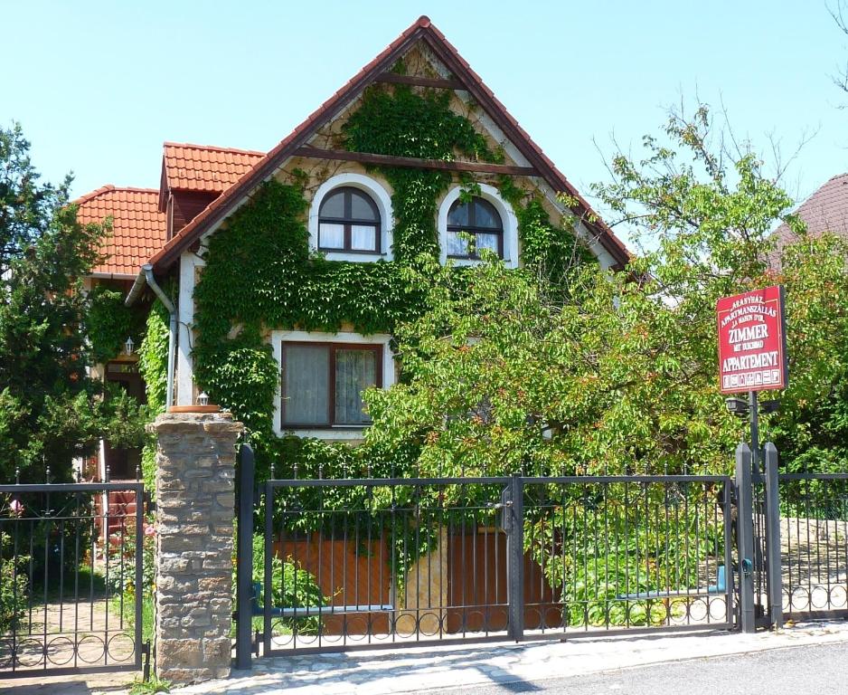 蒂豪尼Aranyház Apartmanszállás的常春藤覆盖的房屋,有栅栏和标志
