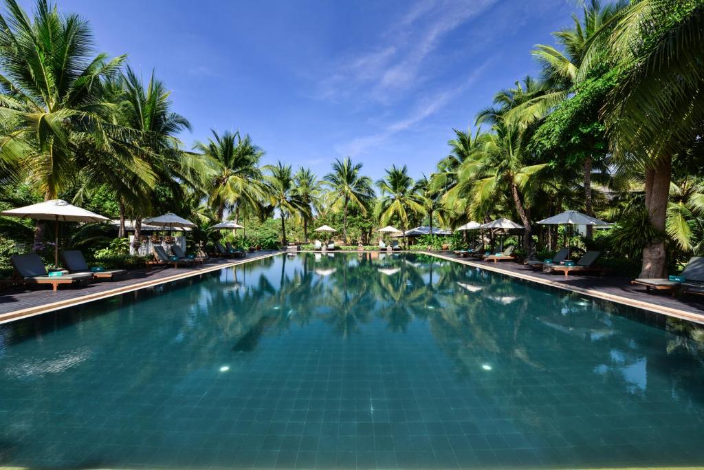 北碧Royal River Kwai Resort and Spa -SHA Extra Plus的一座棕榈树和遮阳伞的大型游泳池