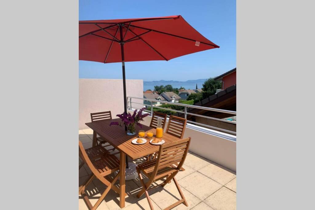 埃维昂莱班Superbe appartement au calme avec vue sur le Lac.的阳台的带红色遮阳伞的天井桌子