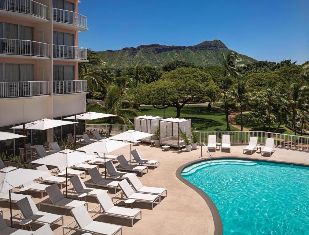 檀香山威基基海岸公园酒店的酒店旁的游泳池设有躺椅和遮阳伞
