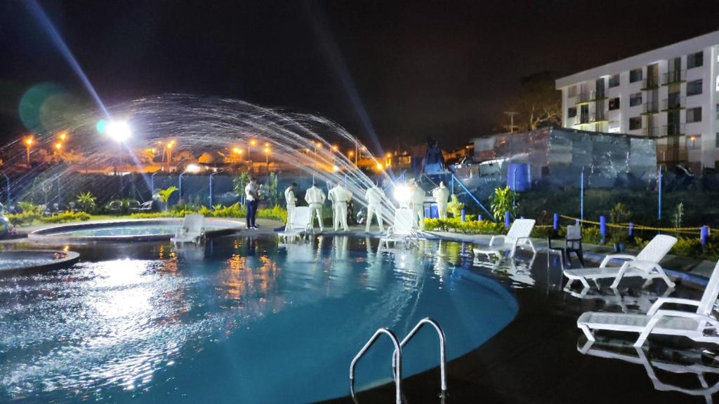 蒙特内哥罗VACACIONES a 3 km del Parque del Cafe的夜间游泳池,设有白色椅子和喷泉