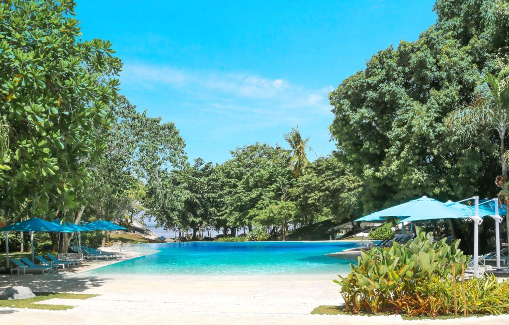 麦克坦Tambuli Seaside Resort and Spa的海滩上的带蓝伞的游泳池