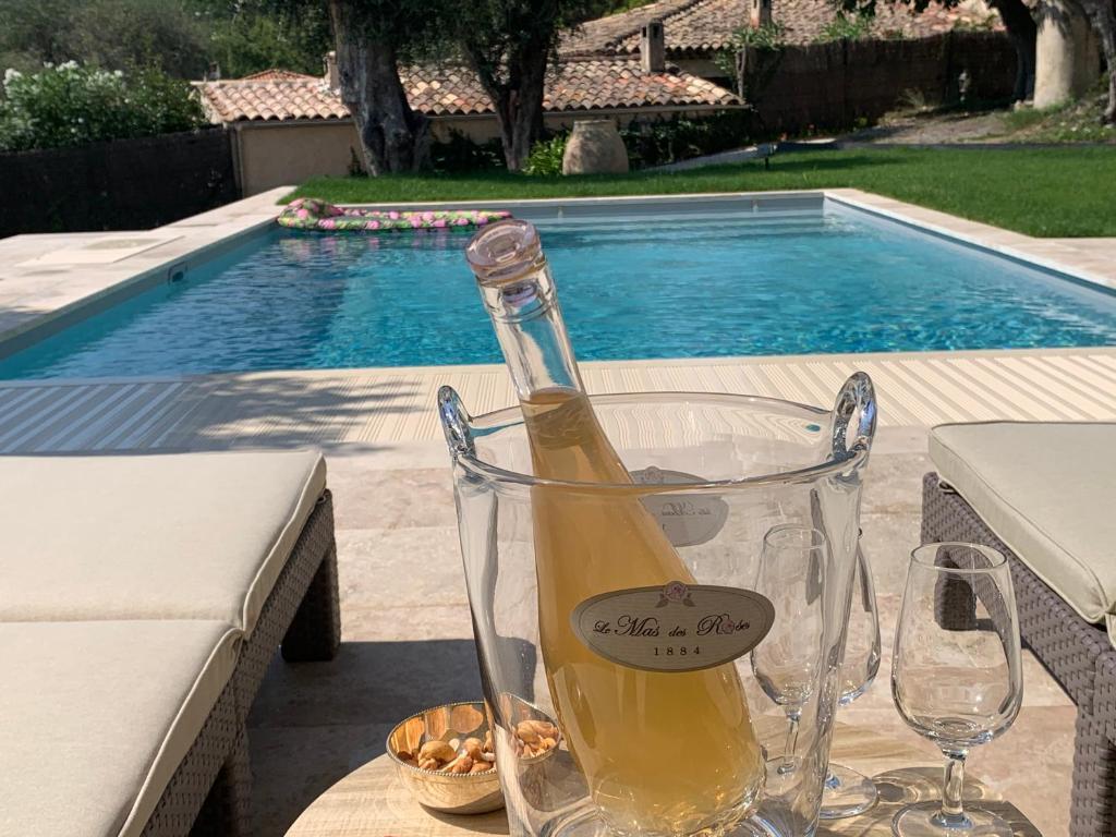 旺斯le mas des roses 1884的游泳池附近的桌子上放着一瓶葡萄酒和两杯酒