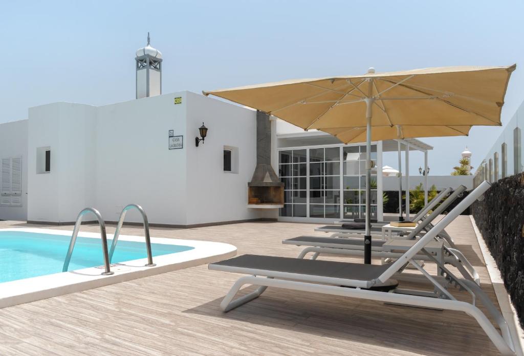卡门港Villas Maribel Pocillos的游泳池旁的天井配有椅子和遮阳伞。