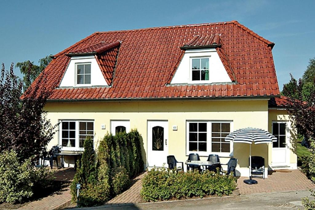 青斯特Am Deich 49的一座带椅子和遮阳伞的红色屋顶房子