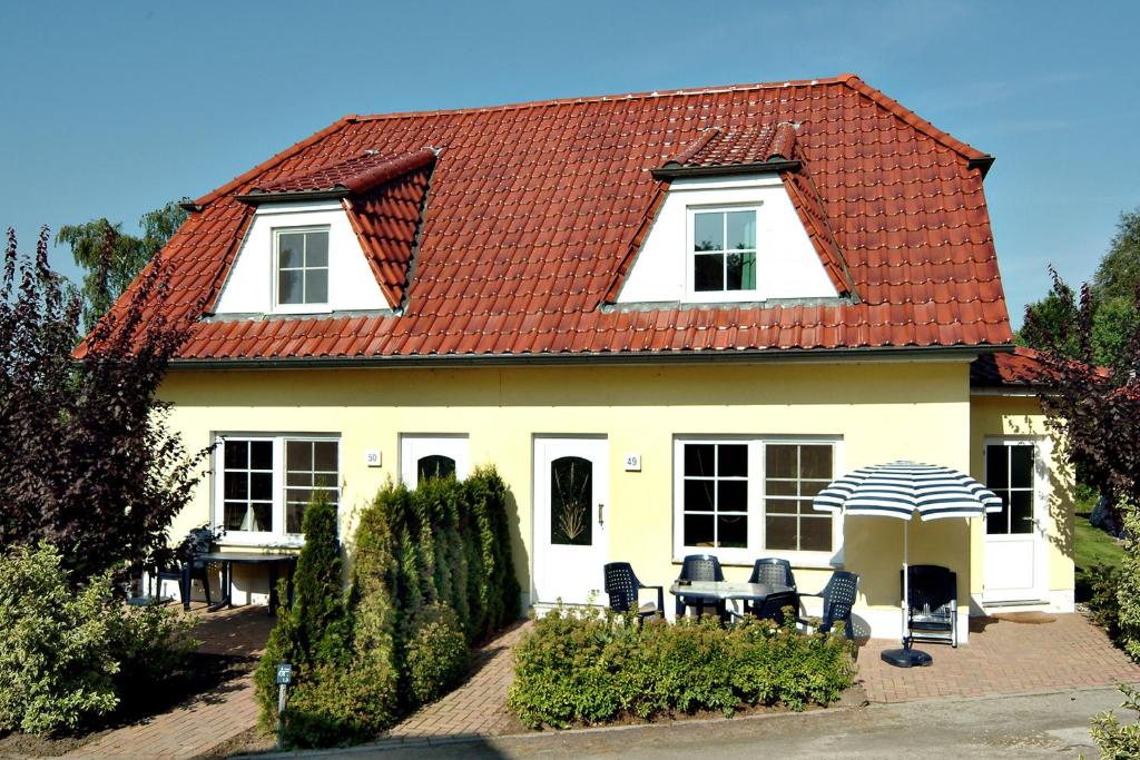 青斯特Am Deich 32的白色的房子,设有红色屋顶,配有椅子和遮阳伞