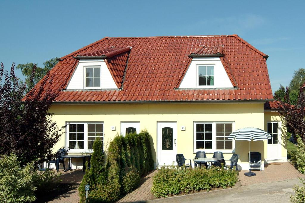 青斯特Am Deich 50的一座带椅子和遮阳伞的红色屋顶房子