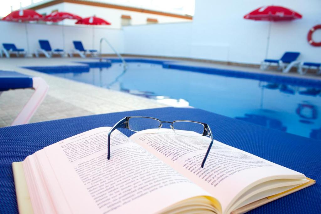 科尼尔-德拉弗龙特拉Villa la Dehesa的坐在游泳池旁桌子上看书,书上戴眼镜