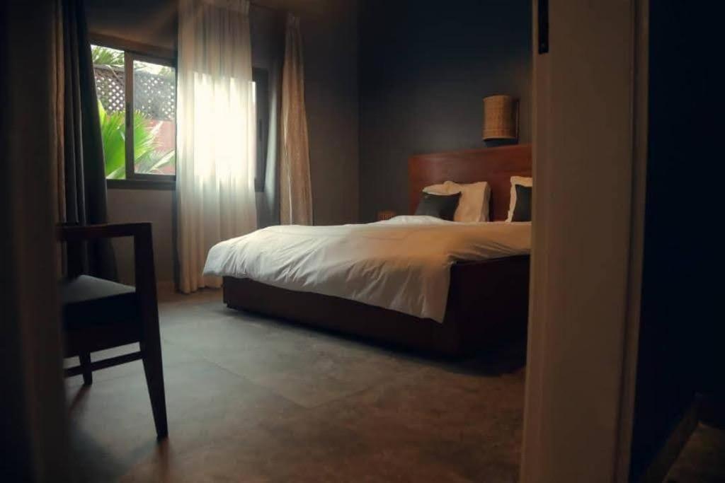 达喀尔O Petit Club Africain Dakar的一间卧室设有一张床、一个窗口和一把椅子