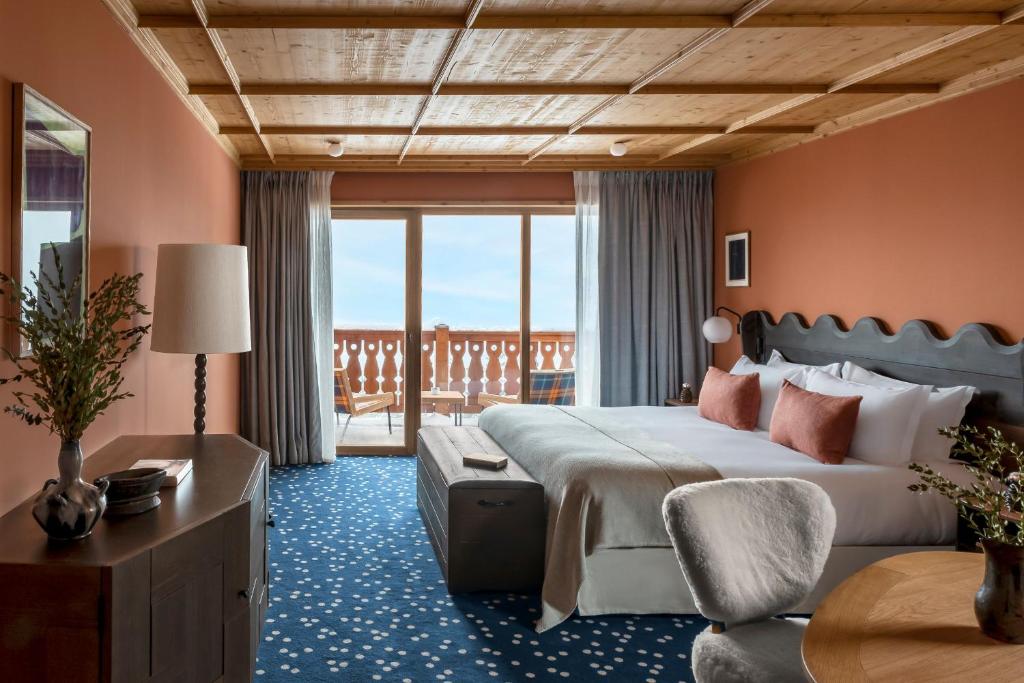 美贝尔Hotel Le Coucou Méribel的一间带大床的卧室和一个阳台