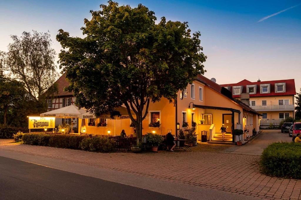 安斯巴赫Hotel-Gasthof Rangau的坐在建筑物旁边的树下的人