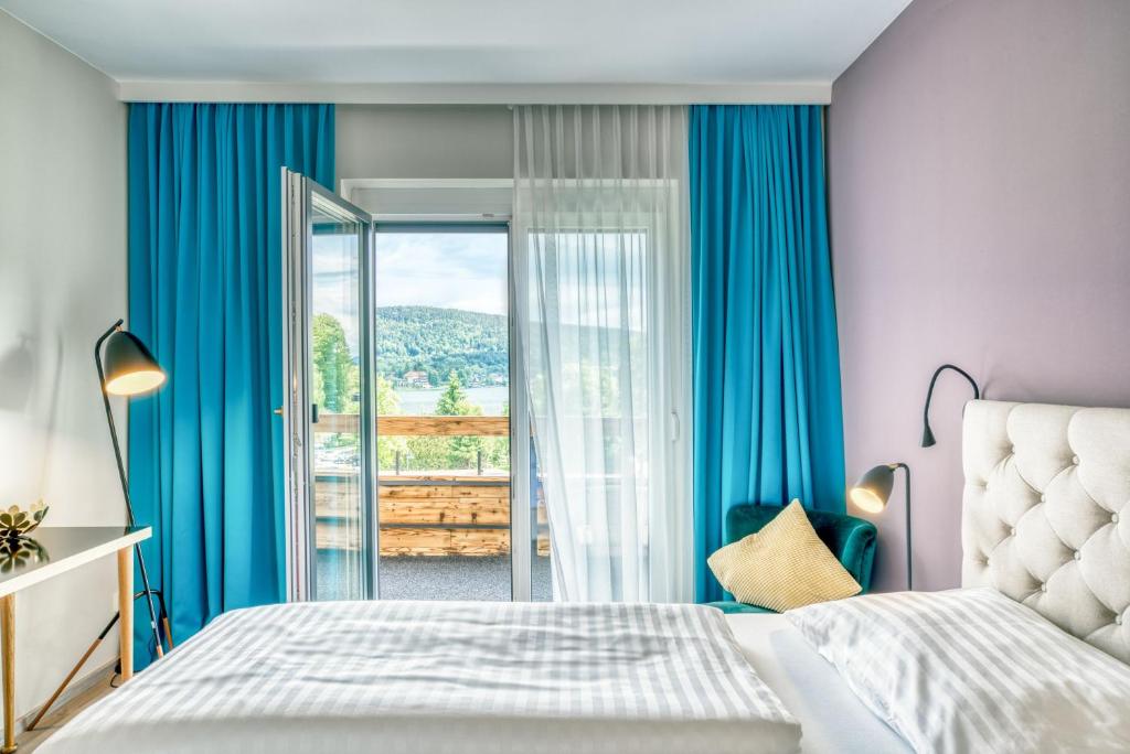 沃尔特湖畔韦尔登Hotel Eden Park的一间卧室配有蓝色窗帘和一张床,并设有一个阳台