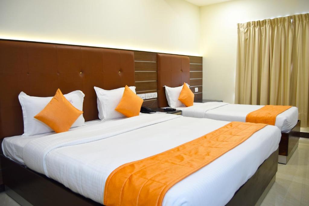 钦奈Thiviyam Airport Hotel的配有橙色枕头的酒店客房内的两张床