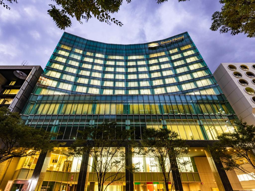 福冈Tenza Hotel at Hakata Station的一座高大的玻璃建筑,前面有树木