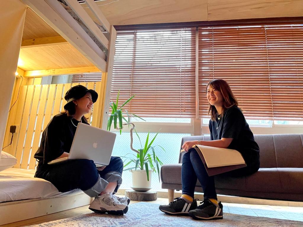 神户Hostel Ini kobe & Donut cafe的两名妇女坐在一张带笔记本电脑的沙发上