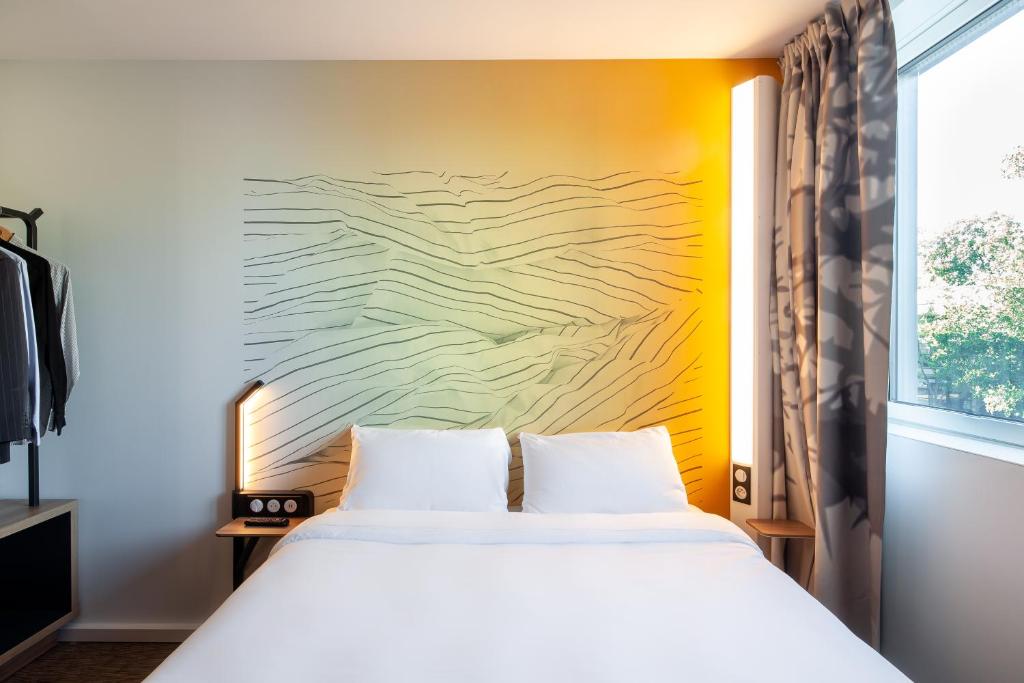 布瓦达西B&B HOTEL Bois d'Arcy Saint Quentin en Yvelines的卧室配有一张床,墙上挂有绘画作品