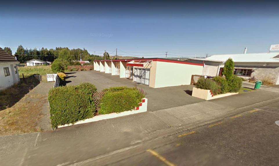 怀乌鲁Roadside Motel的一个空的停车场,有灌木丛和一座建筑