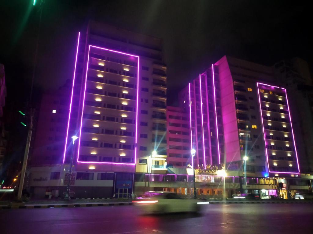 亚历山大26th of July Apartments的两座高楼晚上点亮紫色