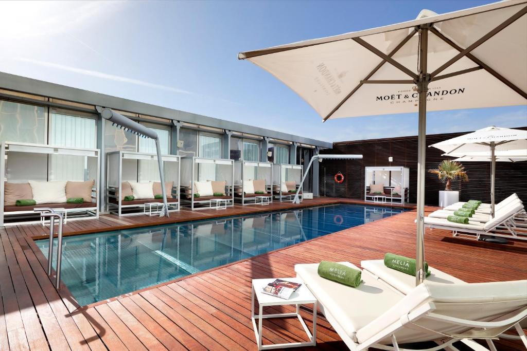 巴塞罗那美利亚巴塞罗那天空四星级酒店的大楼内一个带椅子和遮阳伞的游泳池
