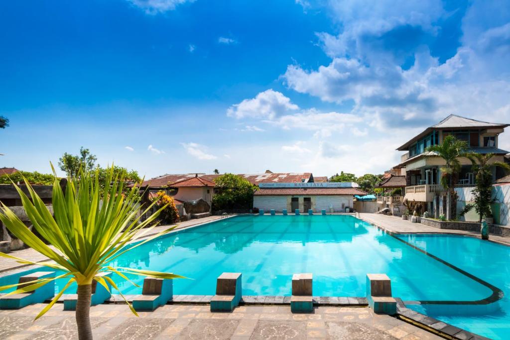 登巴萨登巴萨马哈亚酒店的一座大型游泳池,在房子前有棕榈树