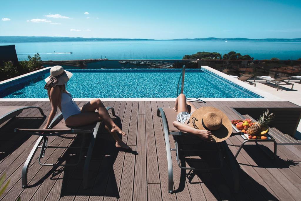 斯普利特马维尔健康酒店的两个女人坐在游泳池旁的椅子上