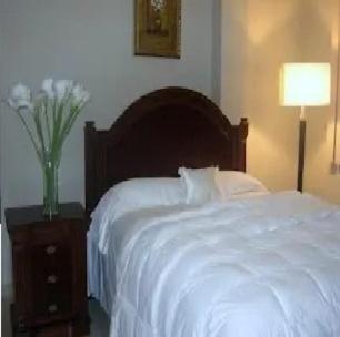 曼塔Hotel Premier Inn的卧室配有白色的床和带花瓶的床头柜