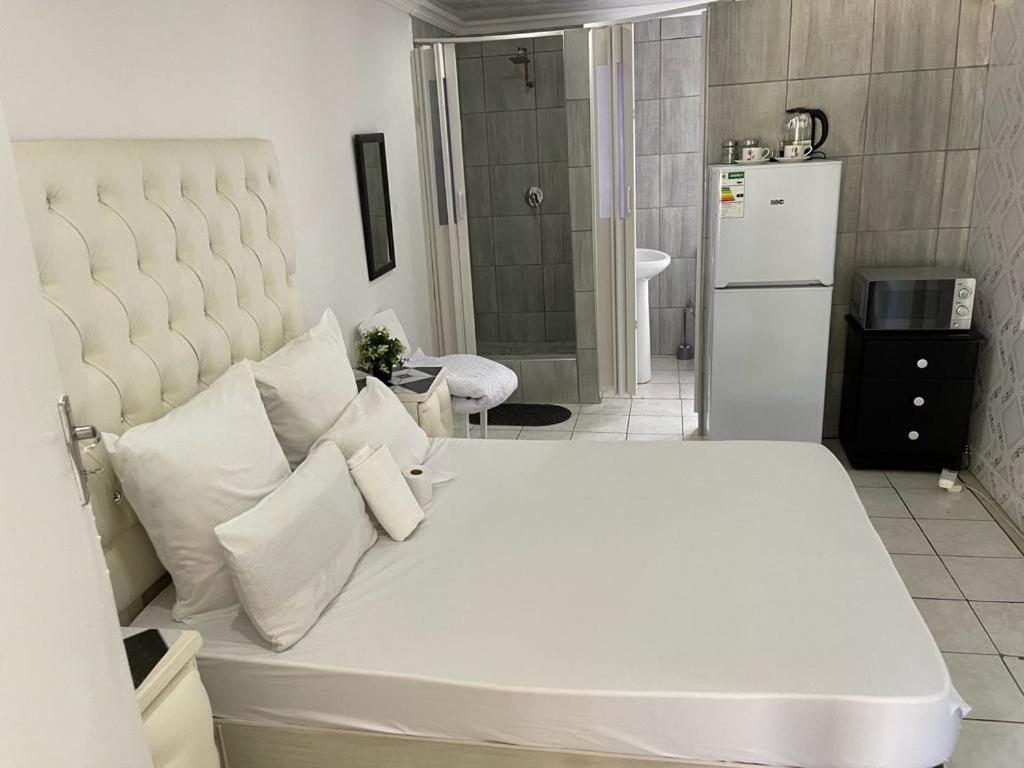 奥克尼Colins Accommodation - DAYREST from R120 OVERNIGHT from R300的卧室配有带枕头的白色床和冰箱。
