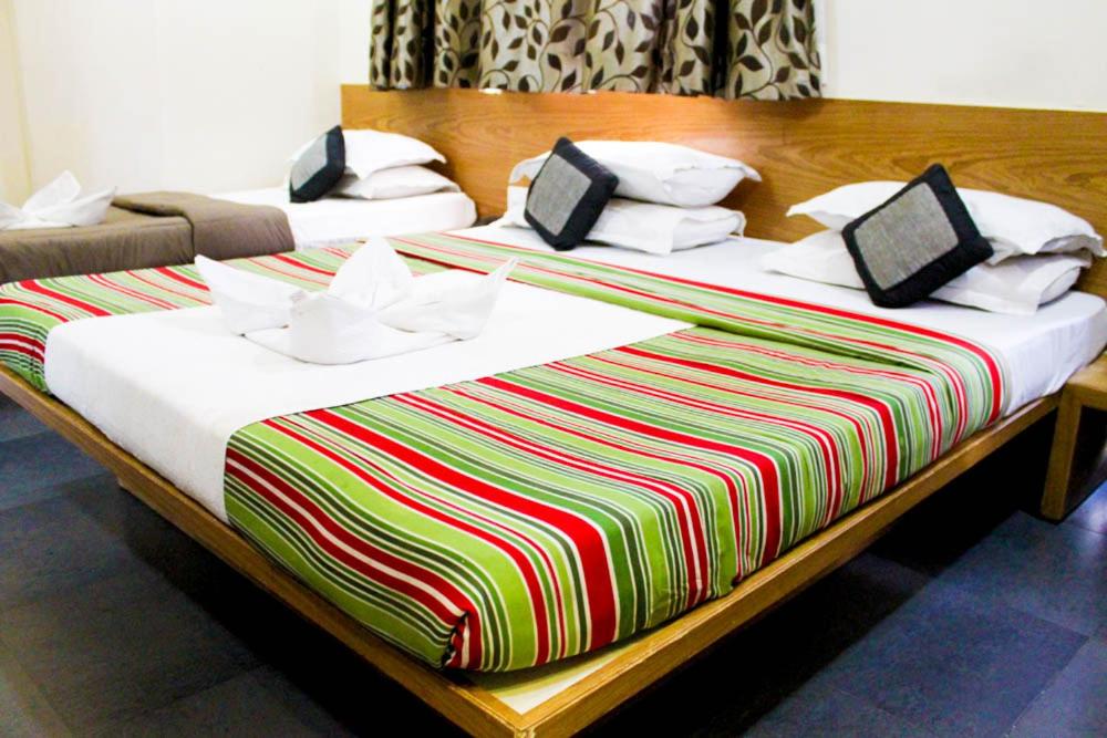 舍地Hotel Shradha Saburi Palace的两张带彩色床单和枕头的床