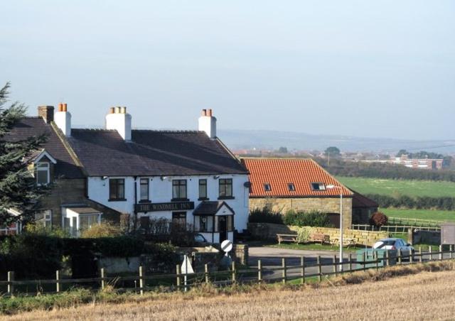 惠特比The Windmill Inn - Whitby的田野旁的白色房子,有栅栏