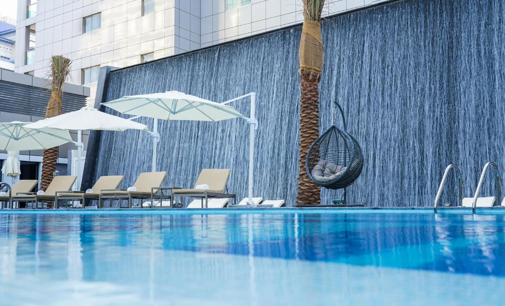 迪拜Al Khoory Sky Garden Hotel的一个带遮阳伞和椅子的游泳池以及一个喷泉