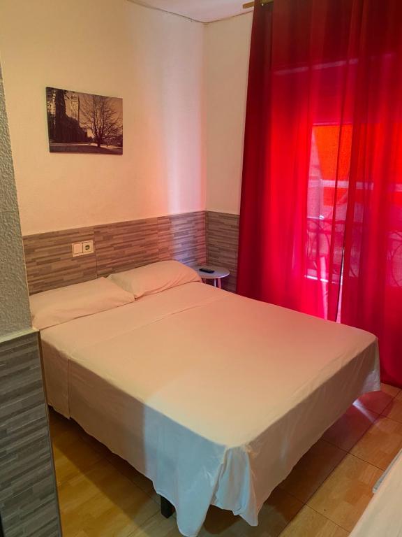 贝尼多姆PENSIÓN ROSA的一间卧室配有一张带红色窗帘的床和一扇窗户