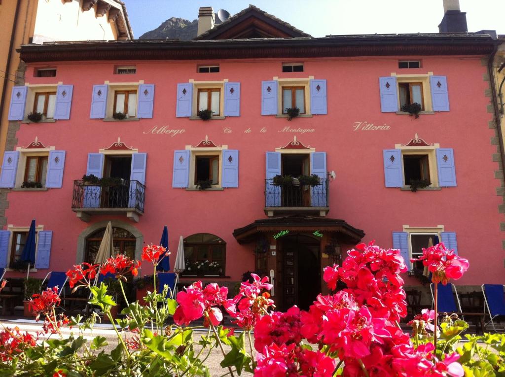 MontesplugaHotel Vittoria - Ca' De La Montagna的前面有鲜花的粉红色建筑