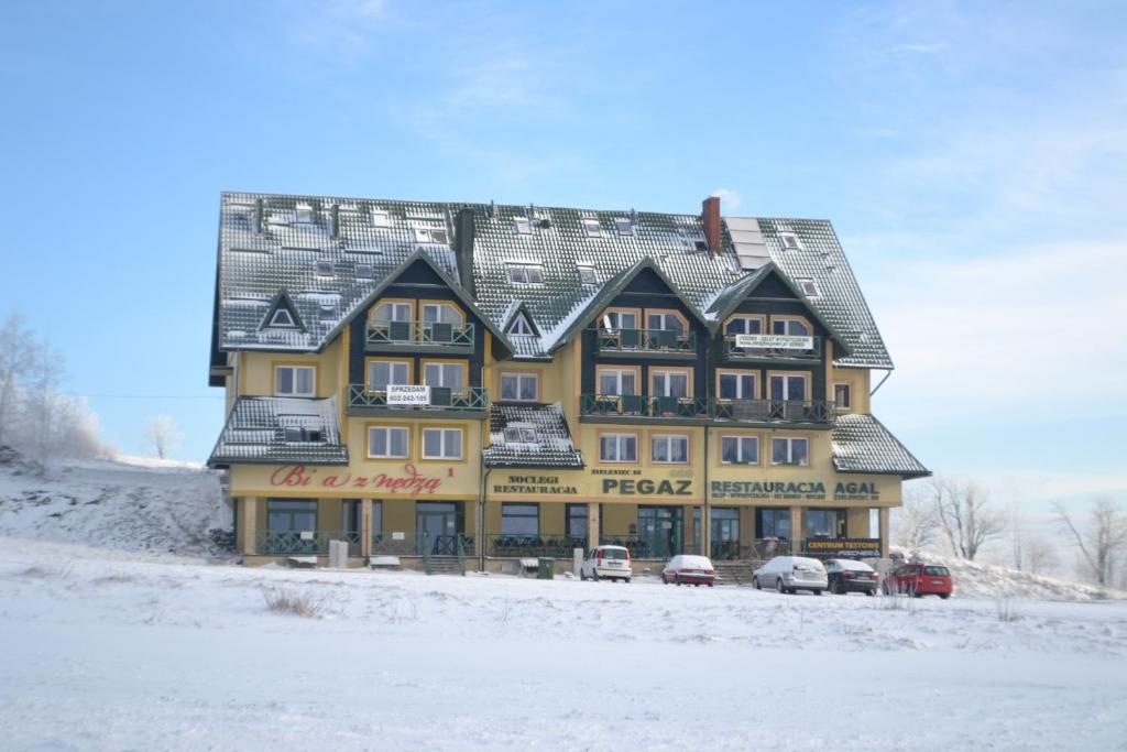 杜什尼基-兹德鲁伊Ośrodek Pegaz的一座大型黄色建筑,汽车停在雪中