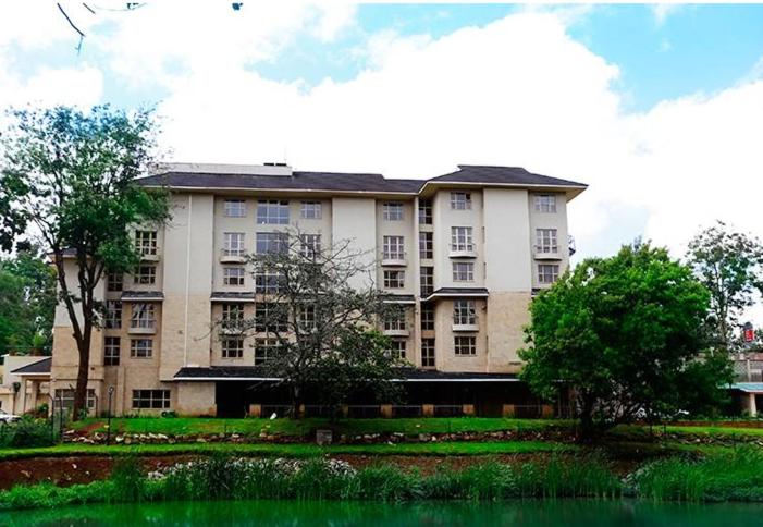 内罗毕Qaribu Inn Boutique Hotel Nairobi的一座大型公寓楼,里面种有树木,设有池塘