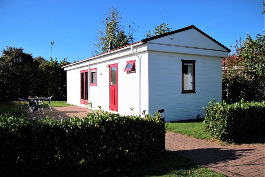 DrijberHofgalow Chalet op camping "De Stal"的白色的小建筑,有红色的门和桌子