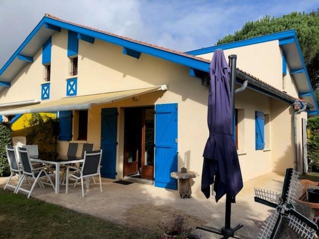 波讷地区圣朱利安Village Océlandes的蓝色和白色的房子,配有桌子和雨伞