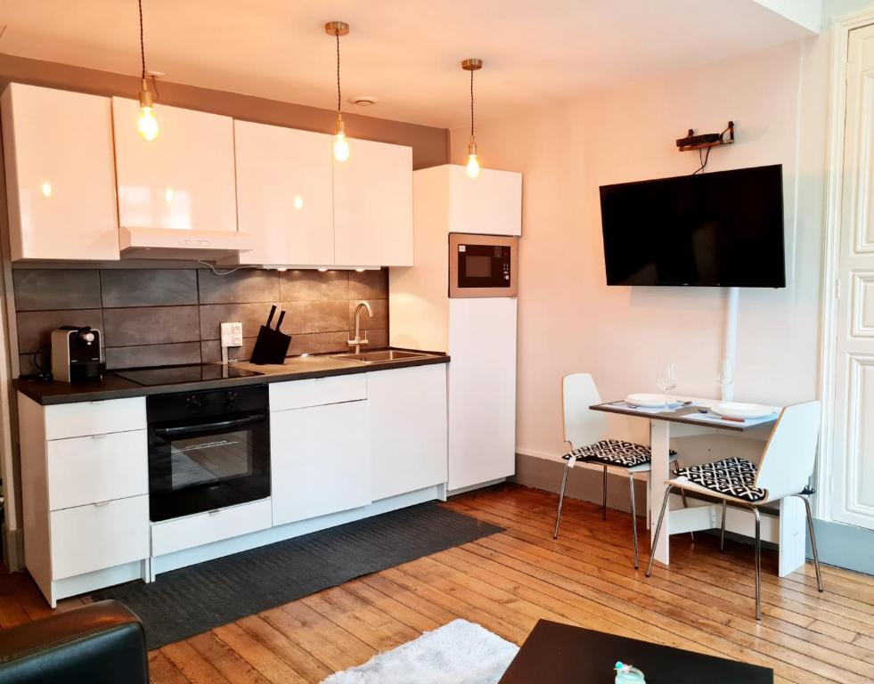 德勒Le Citadin chic的厨房配有白色橱柜、桌子和电视。