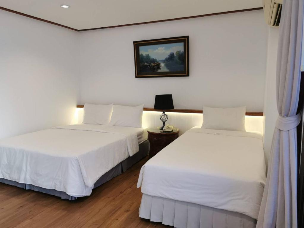 华欣BaanBusarin Hotel的配有白色墙壁和木地板的客房内的两张床