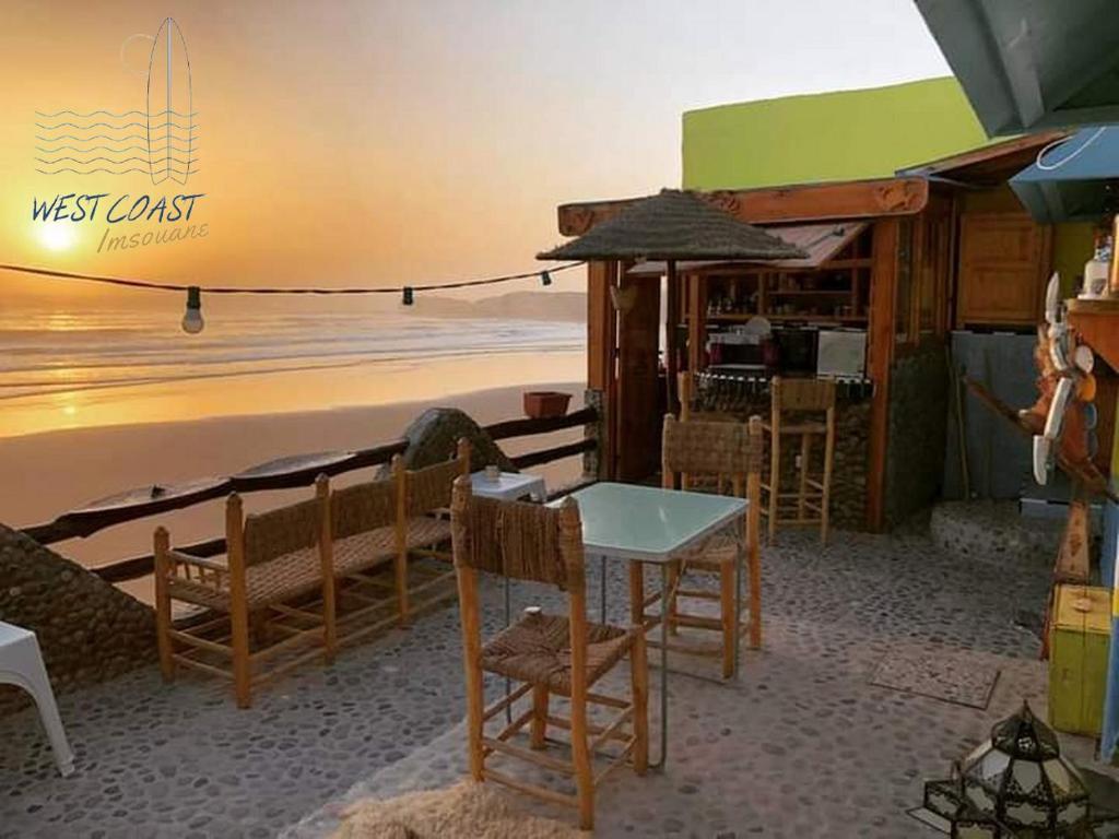 依索安WEST COAST HOSTEL的海滩上的餐厅,配有桌椅