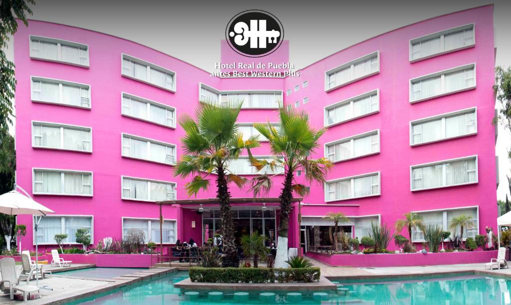 普埃布拉Hotel Real de Puebla的粉红色的建筑,前面有一个游泳池