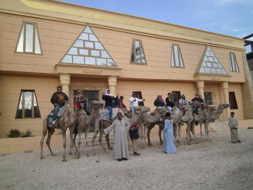 卢克索Pyramids Luxor Hotel & SPA的一群人骑在骆驼上,在一座建筑前
