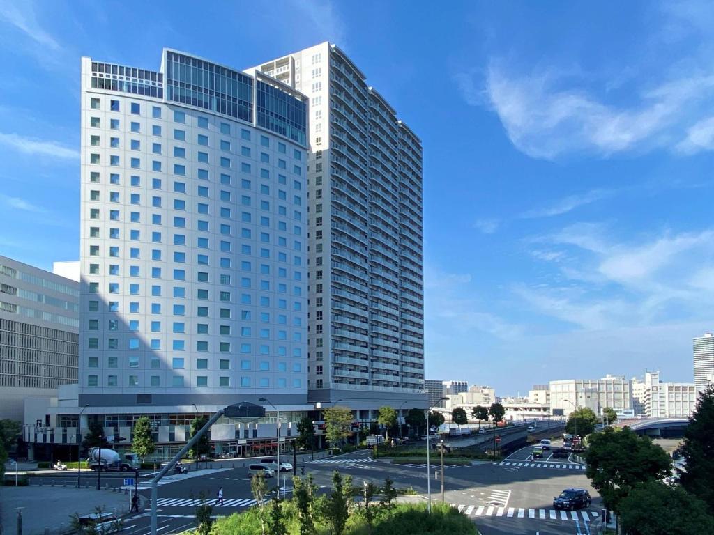 横滨横滨港未来广场酒店(The Square Hotel Yokohama Minatomirai) 的一座高大的白色建筑,前面有一个停车位